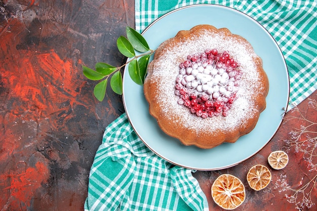 Vista ravvicinata laterale una torta una torta con frutti di bosco e foglie di zucchero sulla tovaglia limone