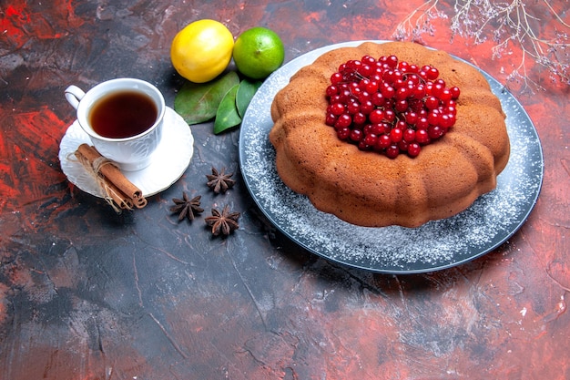 Vista ravvicinata laterale torta torta con ribes rosso sul piatto limone una tazza di tè foglie di anice stellato