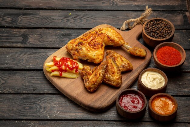 側面のクローズアップビュー鶏肉の食欲をそそる鶏の脚と翼フライドポテトとテーブルの上のカラフルなソースとスパイスのボウル