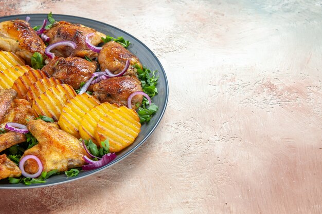 Вид сбоку крупным планом куриные крылышки синяя тарелка аппетитного картофеля куриные крылышки лук зелень