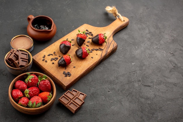 Vista ravvicinata laterale crema al cioccolato fragole e crema al cioccolato e fragole ricoperte di cioccolato sul tagliere della cucina sul tavolo scuro