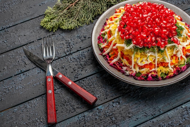 어두운 탁자에 있는 포크 나이프와 가문비나무 가지 옆에 있는 크리스마스 요리를 가까이서 볼 수 있는 크리스마스 요리