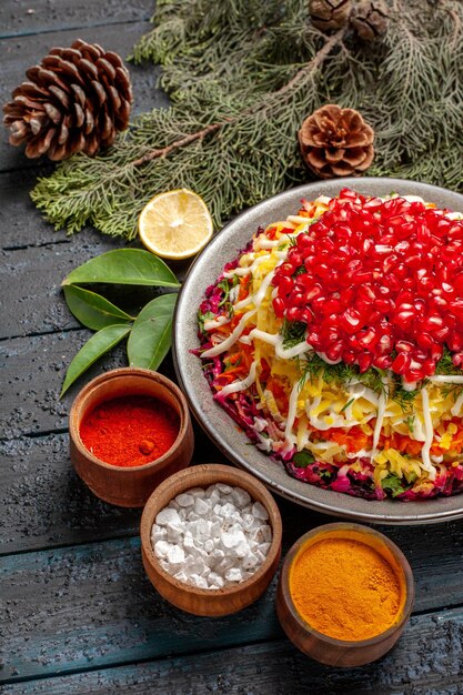 Side close-up view Christmas dish spices lemon spruce branches with cones next to the dish with pomegranates