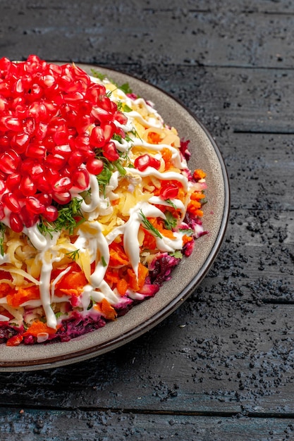 Free photo side close-up view christmas dish tasty christmas salad with seeds of pomegranate mayonnaise and beets in the plate on the wooden table