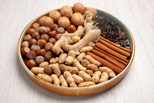 Side close-up view cinnamon sticks cinnamon sticks hazelnuts walnuts peanuts and star anise on the white table