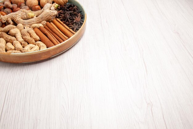 Side close-up view cinnamon sticks peanuts walnuts hazelnuts star anise and cinnamon on the wooden plate on the white table