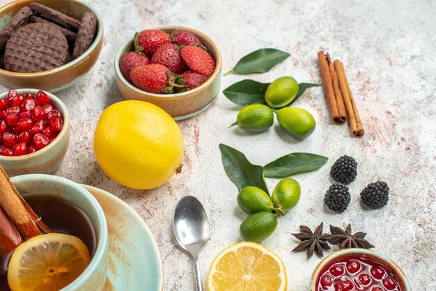 Side close-up view citrus fruits strawberries citrus fruits the appetizing cookies pomegranate lemon spoon a cup of tea with lemon and cinnamon on the table