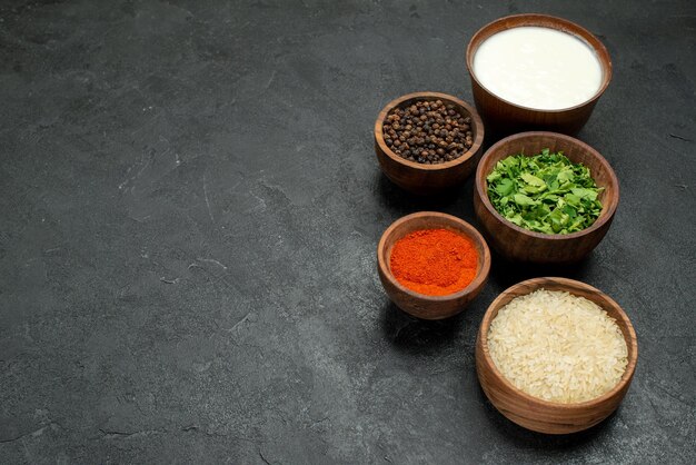 Side close-up view colorful spices plates of colorful spices herbs sour cream rice and black pepper on the right side of wooden table