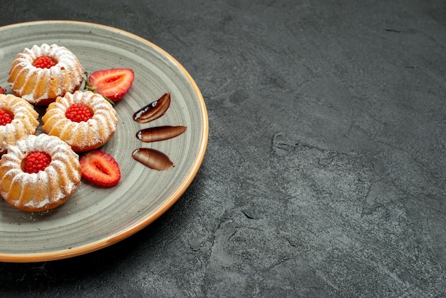 Side close-up view cookies in plate cookies with chocolate and strawberry on white plate on the left side of black table