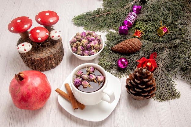 Side close-up view a cup of herbal tea a cup of herbal tea next to the cinnamon branches with Christmas tree toys and cones and pomegranate on the table