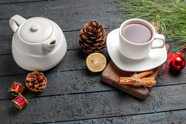 Side close-up view a cup of tea a cup of tea cinnamon sticks lemon and cone next to the cup of tea teapot and Christmas tree branches with toys