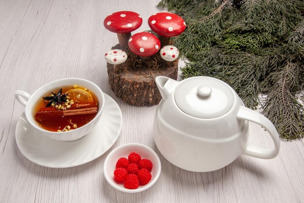 側面のクローズアップビューベリーのお茶の白いティーポットボウルトウヒの枝とクリスマスのおもちゃの横にレモンとお茶のカップ