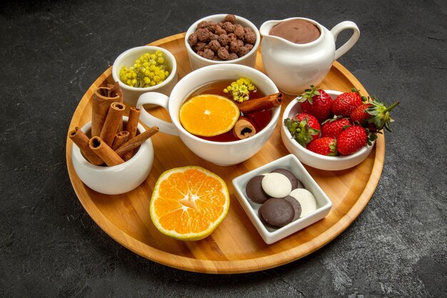 側面のクローズアップビューお菓子チョコレートクリームとお茶のカップレモンイチゴチョコレートと木の板のハイゼルナッツ