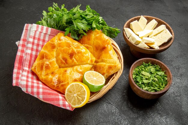 Side close-up view dish in basket bowls of black pepper herbs and cheese and wooden basket of pies lemon herbs and checkered tablecloth on the table