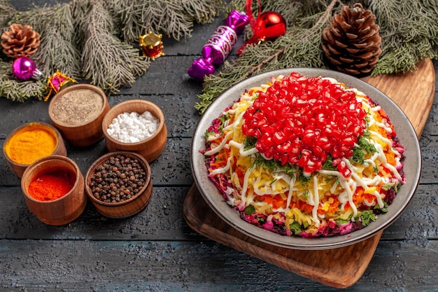 Side close-up view dish of pomegranate dish with pomegranates on the cutting board spices next to the tree branches with cones and Christmas tree toys