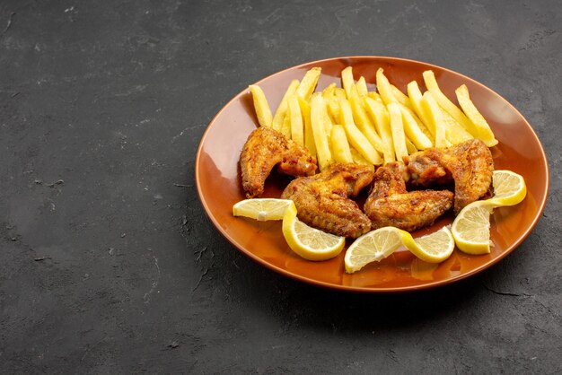 Side close-up view fastfood plate of tasty chicken wings french fries and lemon on the dark background