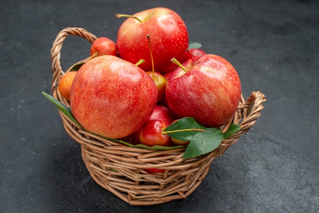 어두운 테이블에 바구니에 잎 측면 확대보기 과일 사과와 체리