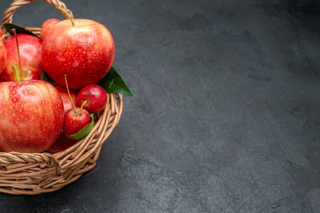 Side close-up view fruits cherries and apples with leaves in the basket on the table