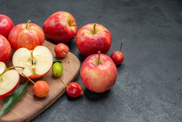 Вид сбоку крупным планом фрукты, фрукты, ягоды на доске рядом с яблоками с листьями