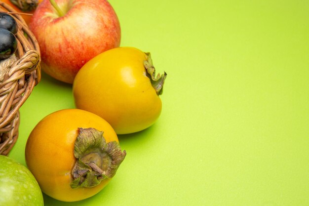 Вид сбоку крупным планом фрукты хурма красное яблоко грозди черного винограда на зеленом столе