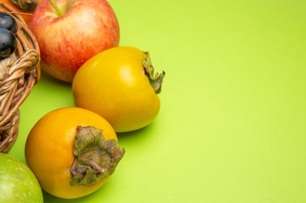 Side close-up view fruits persimmons red apple bunches of black grapes on the green table