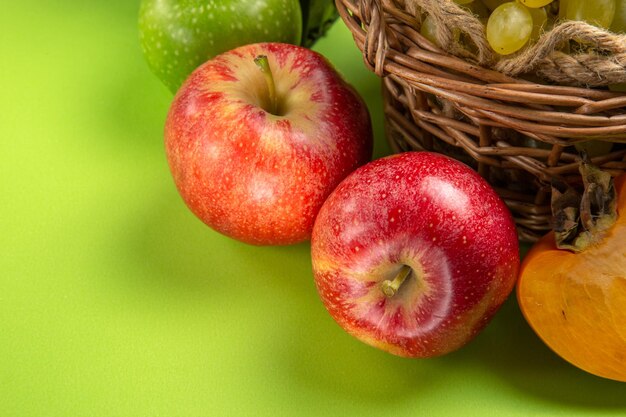 Side close-up view fruits red apples bunches of green grapes persimmon on the green table