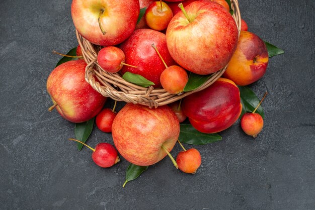 Side close-up view fruits red-yellow fruits and berries with leaves in the wooden basket