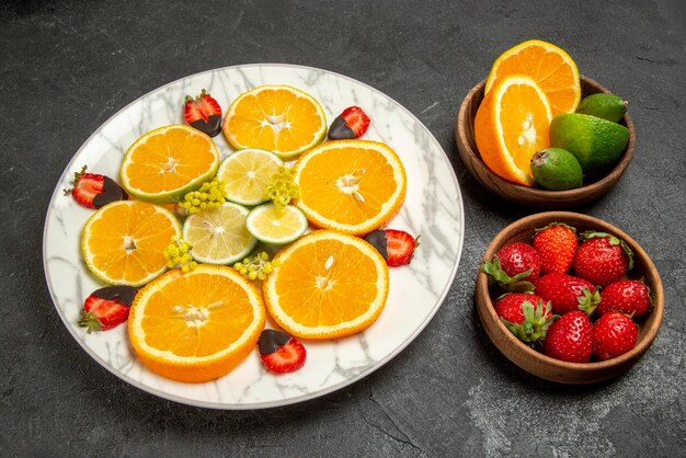 チョコレートで覆われたイチゴと柑橘系の果物のプレートの横にある柑橘系の果物とベリーのテーブルプレート上の果物の側面のクローズアップビュー