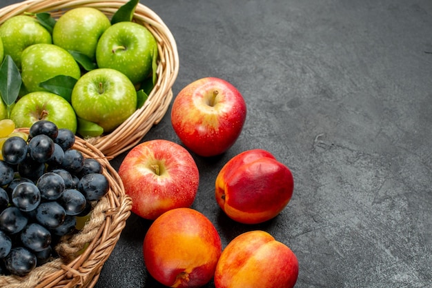 Side close-up view fruits wooden baskets of green apples and bunches of grapes nectarines