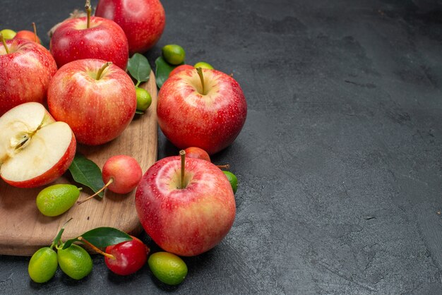 Side close-up view fruits yellow-red apples and cherries with leaves on the board citrus fruits