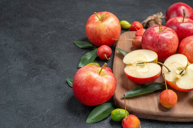 Side close-up view fruits yellow-red cherries with leaves apples on the board citrus fruits