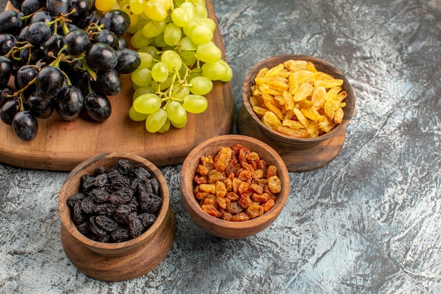 Foto gratuita vista ravvicinata laterale uva marrone ciotole di frutta secca e grappoli d'uva sulla tavola della cucina