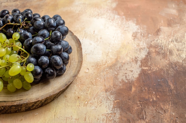 Free photo side close-up view grapes bunches of black and green grapes on the cutting board