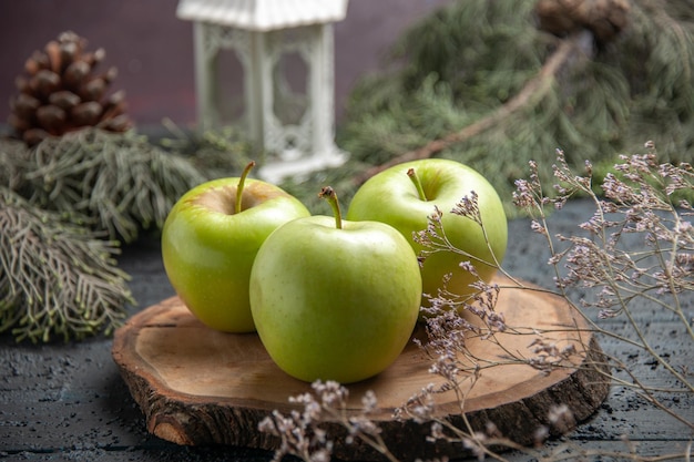 측면 클로즈업 보기 녹색 사과는 원뿔이 있는 나뭇가지 옆에 있는 갈색 판자에 3개의 사과를 먹습니다.