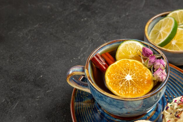 Side close-up view herbal tea herbal tea with lemon and cinnamon sticks in the blue cup next to the bowl of slices of lime on the dark table