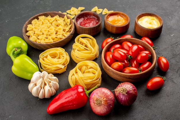 Side close-up view pasta and tomatoes red and green bell pepper onion garlic three kind of sauces next to the bowls of pasta and tomatoes on the table