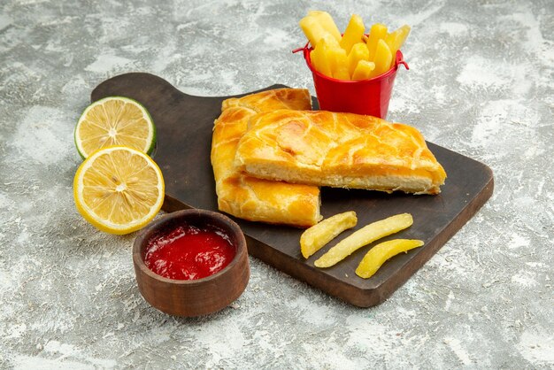 Side close-up view pies french fries bowl of ketchup lemon and french fries and appetizing pies on the kitchen board on the grey table