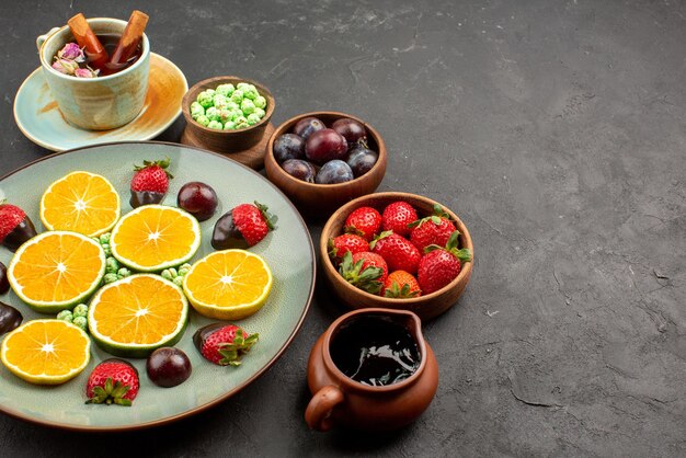 テーブルの左側にあるフルーツチョコレートで覆われたストロベリーグリーンキャンディーみじん切りオレンジとチョコレートソースとベリーのボウルの側面のクローズアップビュープレート