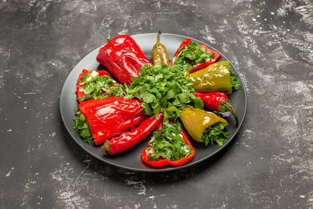 Free photo side close-up view plate of peppers peppers with herbs on the dark plate