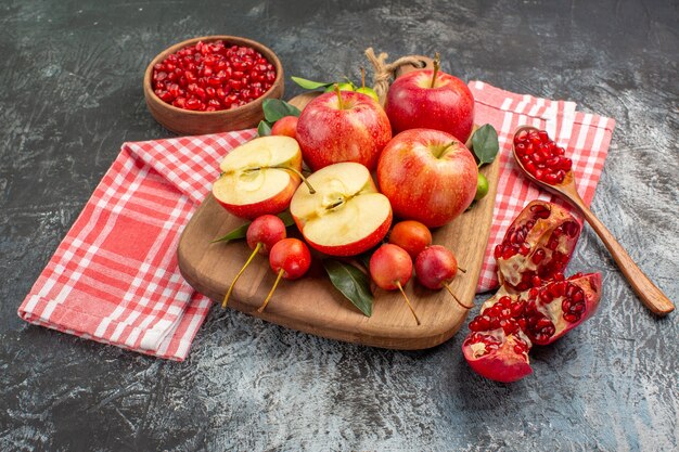 Side close-up view pomegranate apples cherries on the cutting board bowl of pomegranate