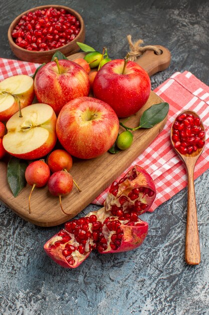 Side close-up view pomegranate pomegranate spoon apples cherries on the wooden board