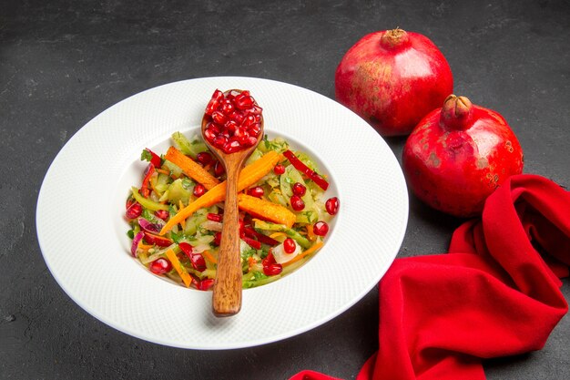 Side close-up view pomegranate two pomegranates vegetable salad spoon with seeds of pomegranates