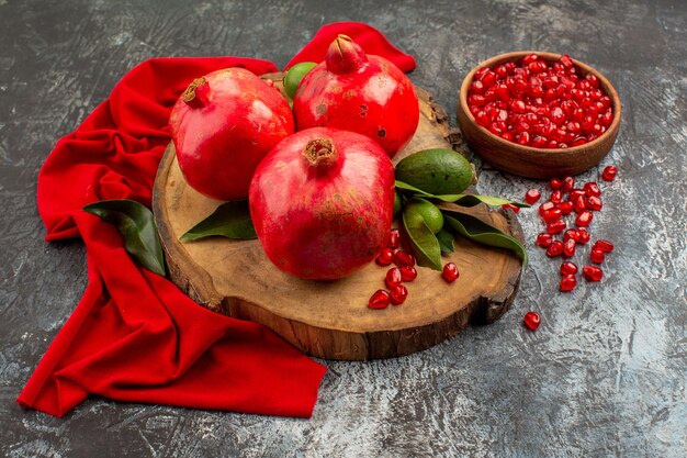 Side close-up view pomegranates pomegranates on the board next to the bowl of pomegranate seeds