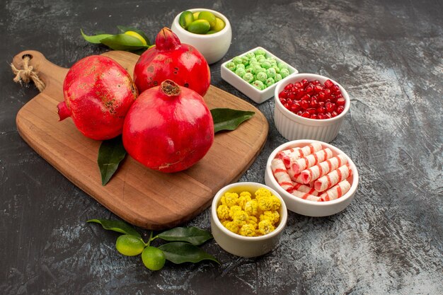 Side close-up view pomegranates pomegranates on the cutting board colorful candies citrus fruits