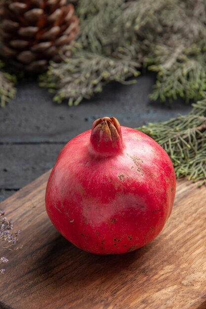 Side close-up view ripe pomegranate red pomegranate on cutting board next to the spruce branches with cones on grey table