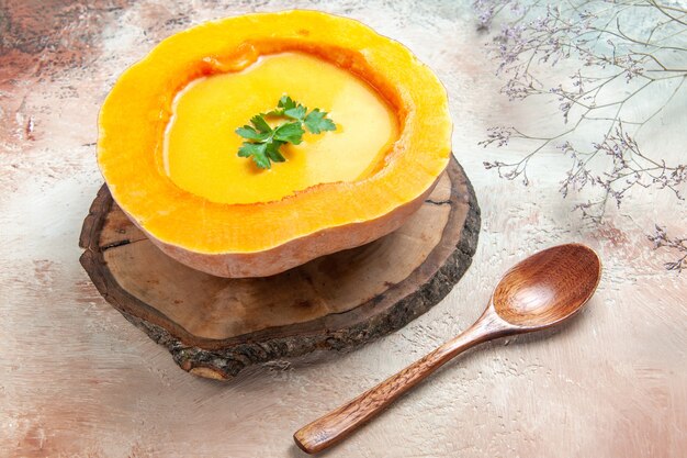 Side close-up view a soup pumpkin soup on the board next to the spoon tree branches