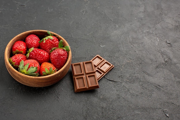 Side close-up view strawberries in bowl strawberries in bowl next to bars of chocolate on the dark table