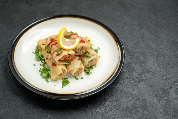 Side close-up view stuffed cabbage stuffed cabbage with herbs lemon and sauce on plate in the center of black table