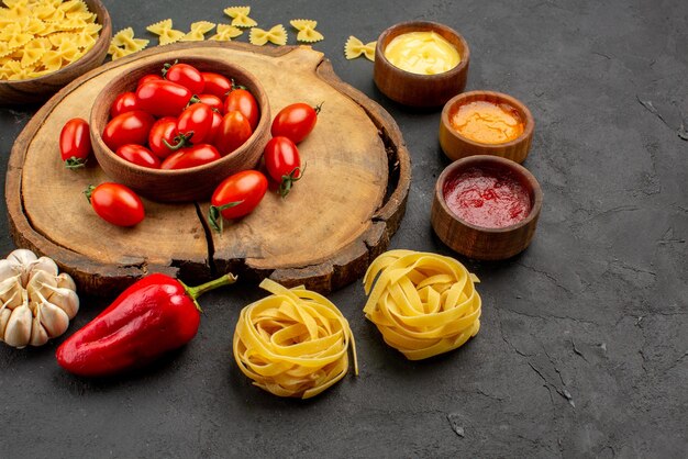 Side close-up view tasty food pasta with three kind of sauces onion bell pepper and garlic next to the bowl of tomatoes on the wooden cutting board