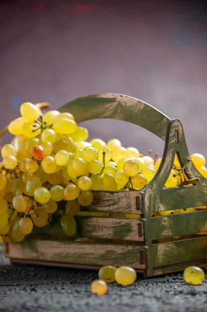 Side close-up view white grapes bunch of white grapes in wooden box on dark table next to spruce branches